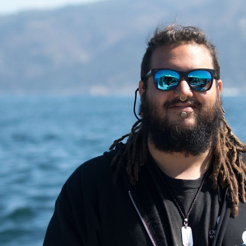 a man wearing sunglasses and standing next to a body of water