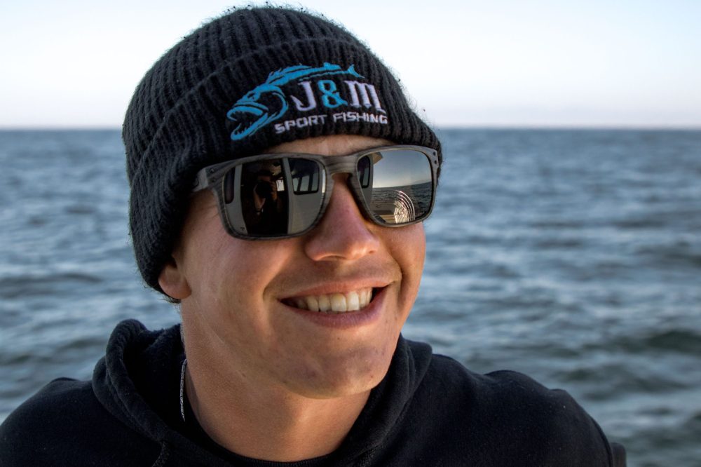 a man wearing a hat and sunglasses in front of a body of water