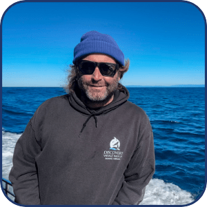 Man in blue beanie and sunglasses on a boat with ocean background.